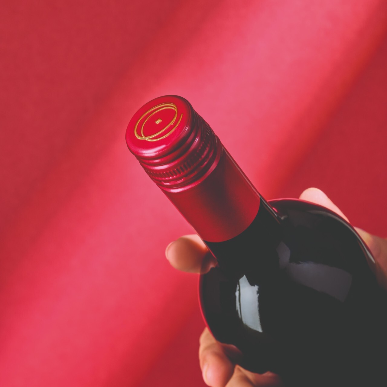 Wine bottle with a red screw cap against a red background.