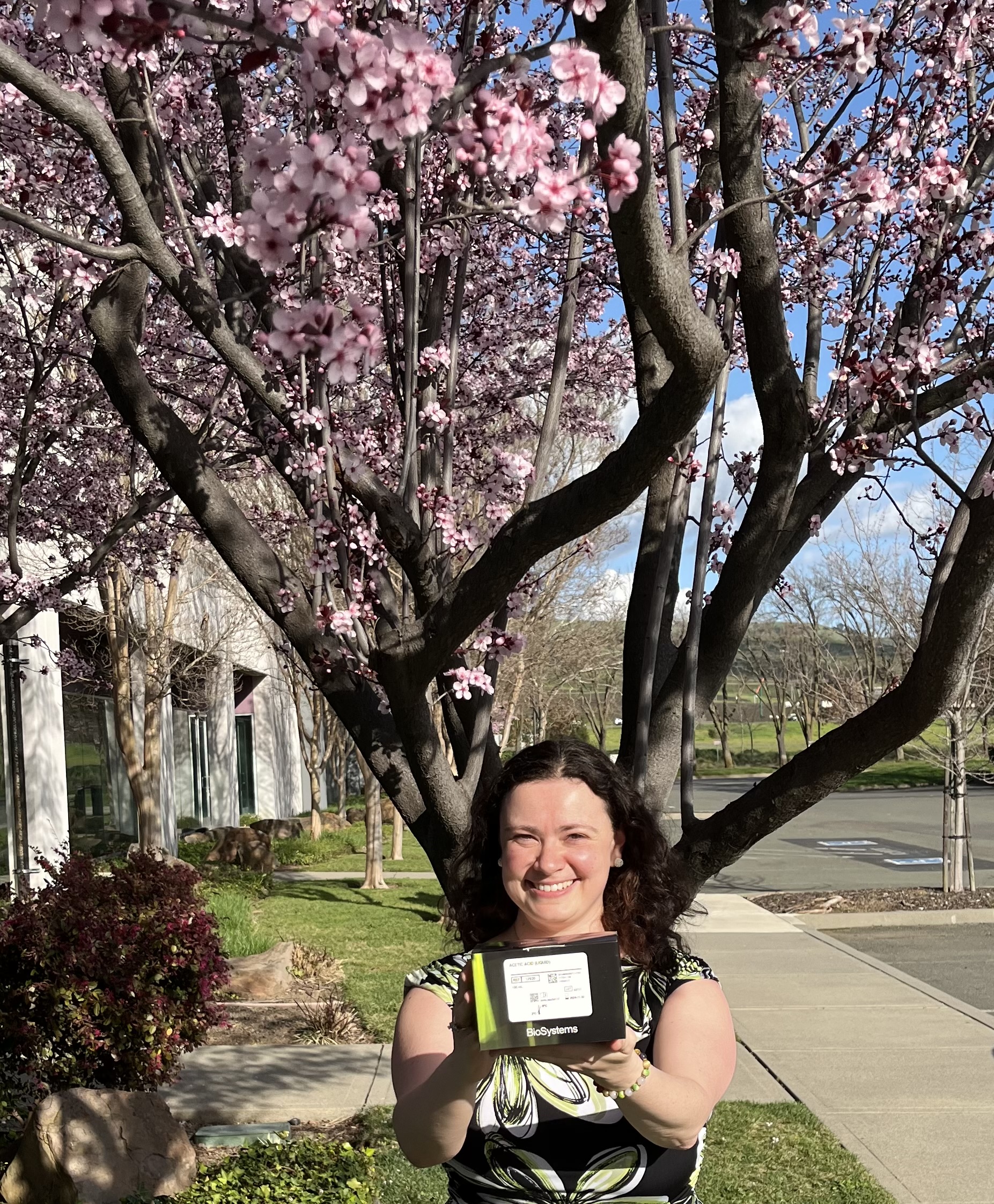 Lauren Armanino with Admeo reagent box in front of a flowering tree and with a bright blue sky